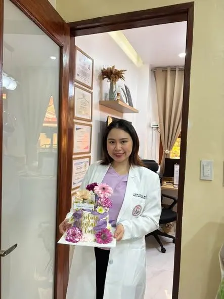 The dentist in a white coat holding the clinic’s 7th-anniversary cake