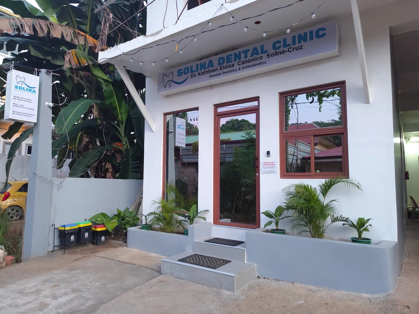 The white clinic with the blue Solina Dental Clinic sign and potted plants by the steps
