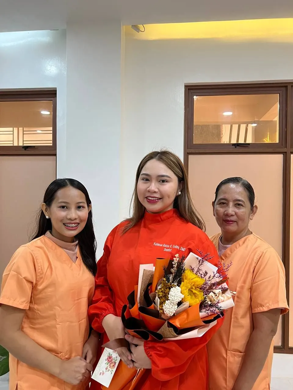 Three women from the clinic smiling with a bouquet in the treatment room